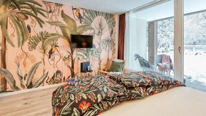 A bedroom with a large bed, a television, and a view of a snowy landscape through a sliding glass door. - Apartment Rio (Winterberg)