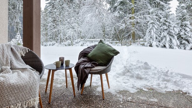 A covered outdoor seating area with a wicker chair and table, a green cushion, and two mugs. - Apartment Rio (Winterberg)