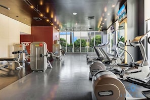 A gym with treadmills, weight machines, and a large window offering a view of greenery and buildings. - Near Beach|Infinite View|Balcony|Pool+ Gym (Hallandale Beach)