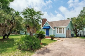 A single-story house with a blue door and a chimney, surrounded by lush greenery. - Coastal Retreat in Rockport Home (Rockport)