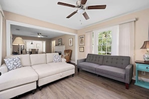 A living room with a beige sofa, a grey sofa, a ceiling fan, and a window with curtains. - Coastal Retreat in Rockport Home (Rockport)