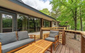 A deck with a sofa and chairs, a wooden table, and a railing overlooking a wooded area.