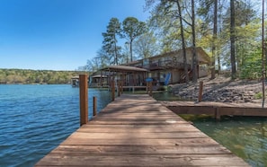 Une jetée en bois menant à une propriété au bord du lac, comprenant une maison et un espace abrité.