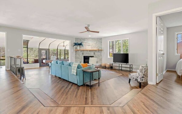 A spacious living area with a stone fireplace, a large sofa, a television, and a ceiling fan.