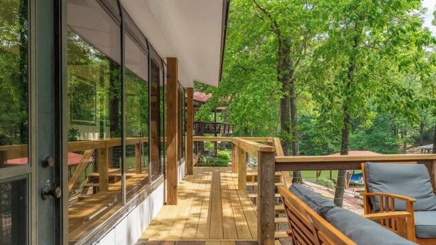 A wooden deck with a view of trees, a wooden bench, and a glass wall.