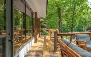 A wooden deck with a view of trees, a wooden bench, and a glass wall.