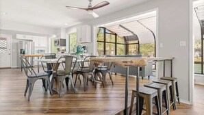 A spacious kitchen with a dining area, large windows, and a ceiling fan.
