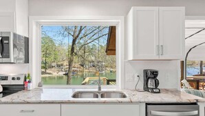 A kitchen with a view of a dock and trees, a coffee maker, and a microwave.