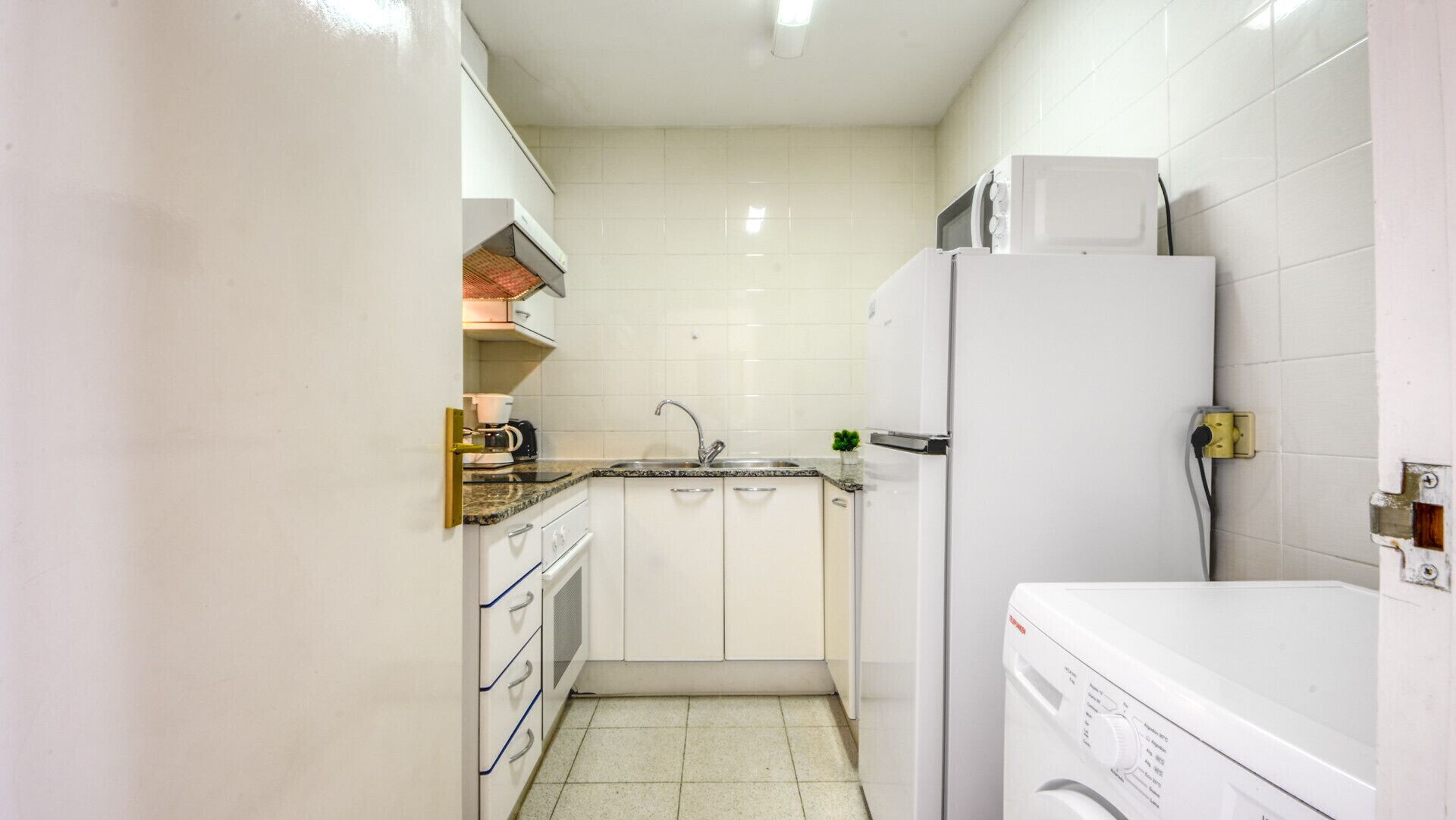 A compact kitchen with white cabinets, a sink, a microwave, and a washing machine.