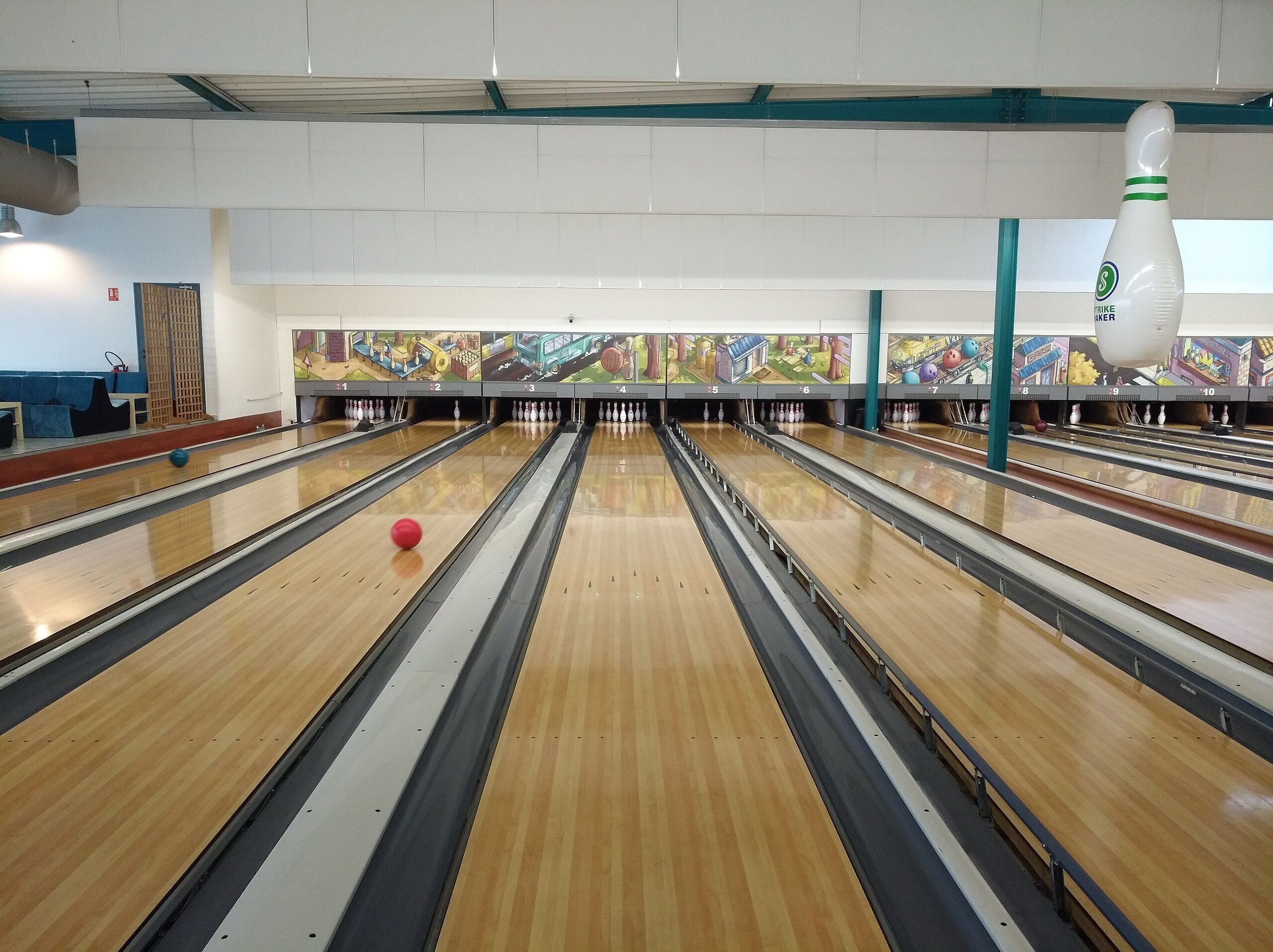 A bowling alley with multiple lanes, a bowling ball in motion, and a bowling pin set up at the end of the lanes.