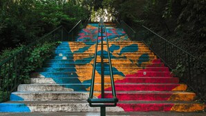 Un escalier dont les marches, peintes à la main dans des couleurs vives, mènent à une main courante en métal.
