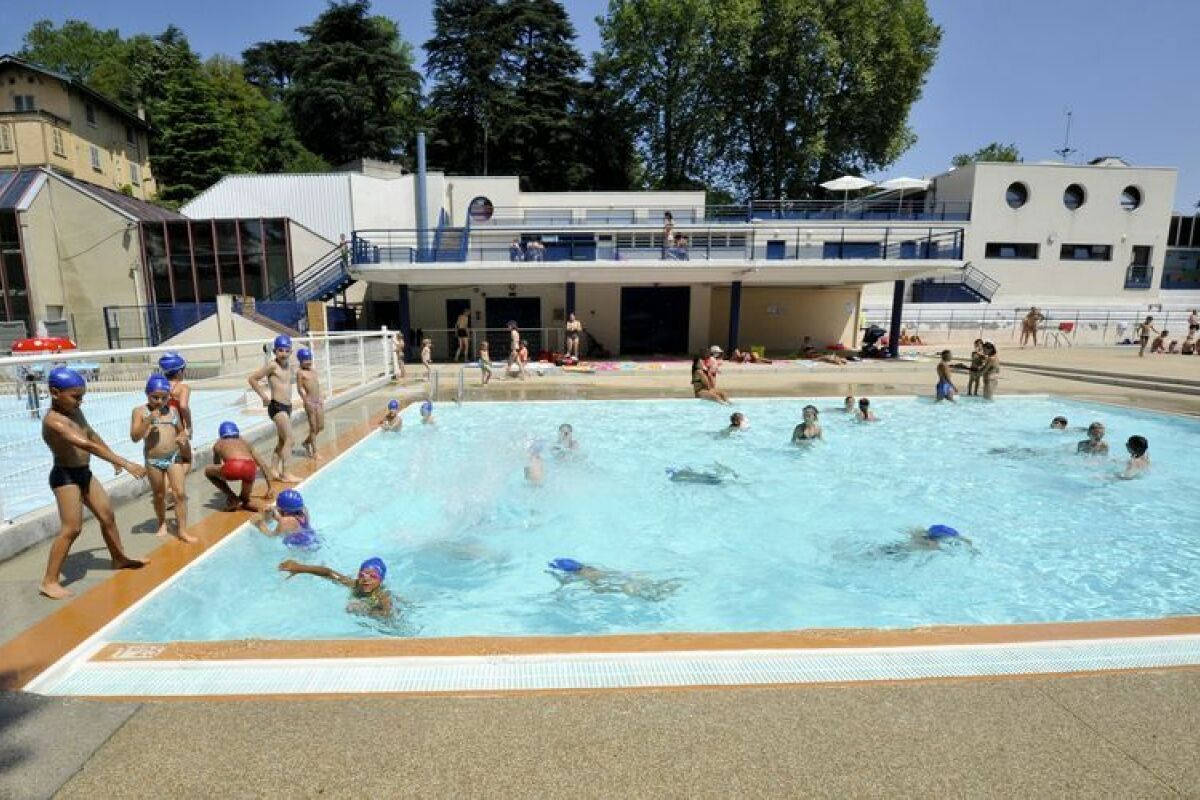 Piscina com pessoas nadando e brincando, cercada por um edifício com varanda e escada.