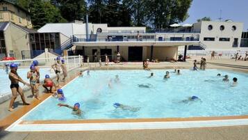 Piscina com pessoas nadando e brincando, cercada por um edifício com varanda e escada.