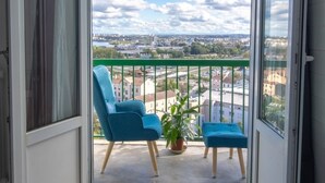 Un balcon avec deux chaises bleues et une petite table, une plante en pot et une vue sur la ville.