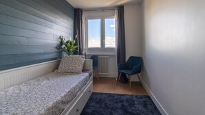 Une petite pièce, bien rangée, avec un lit, une chaise, une fenêtre avec des rideaux et un radiateur.