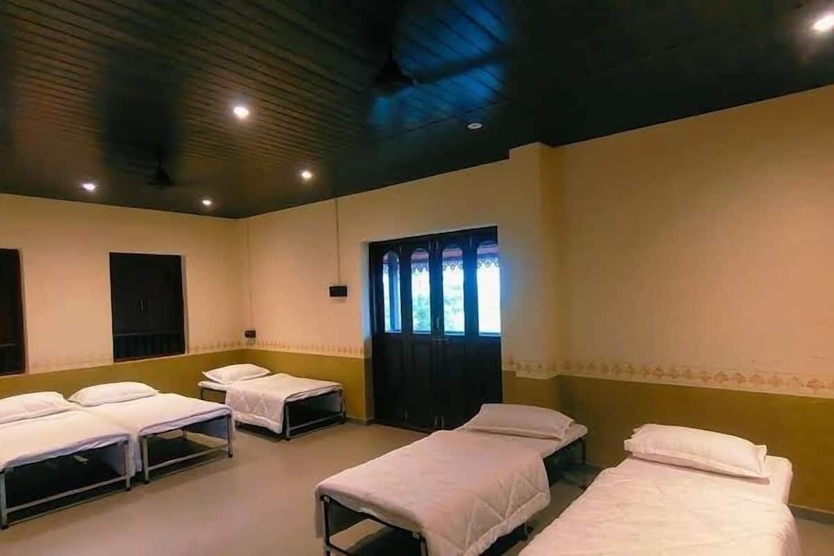 Quarto com quatro camas dispostas em linha, janela com cortinas e iluminação embutida no teto.