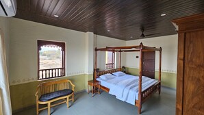 A four-poster bed with a wooden frame, a bench with a cushion, and a window with a decorative frame. - Apla Wada (Khandala)
