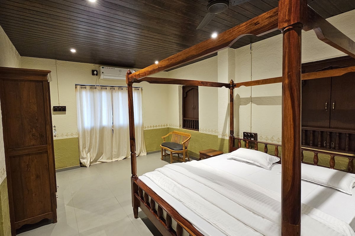 Uma cama de dossel com roupa de cama branca, um guarda-roupa de madeira, uma cadeira e uma janela com cortinas.