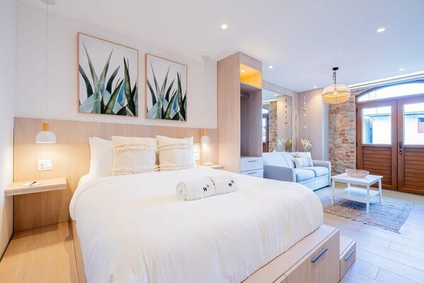 A modern hotel room with a large bed, a sitting area with a sofa and coffee table, and artwork on the walls.