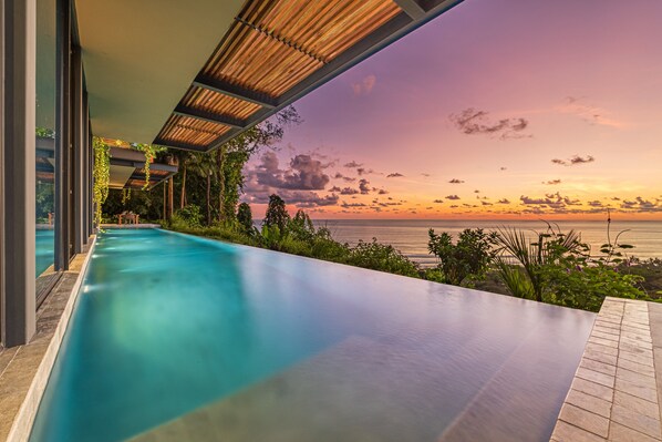Relax by the infinity pool overlooking the ocean and lush greenery.