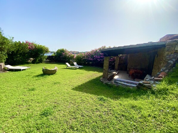 A well-maintained grassy backyard with a stone-built outdoor seating area and a pergola.