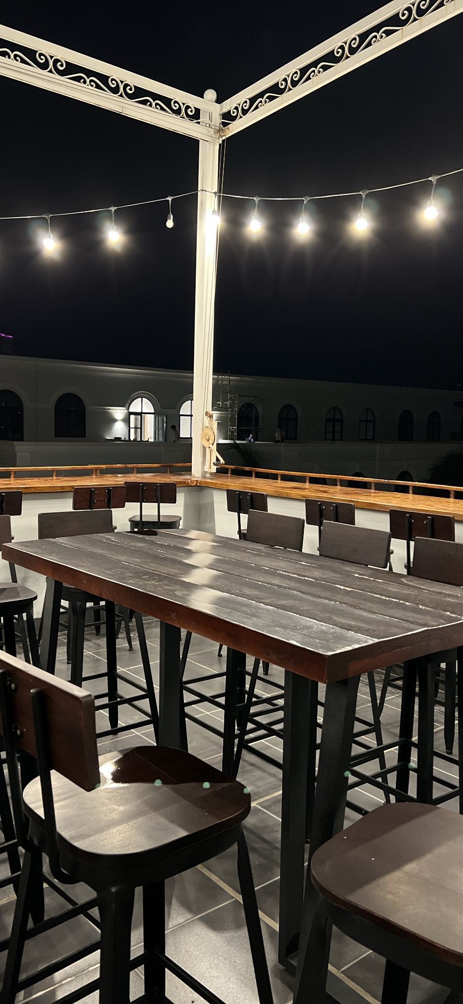 An outdoor dining area with a long table and chairs, surrounded by a white railing with decorative elements.