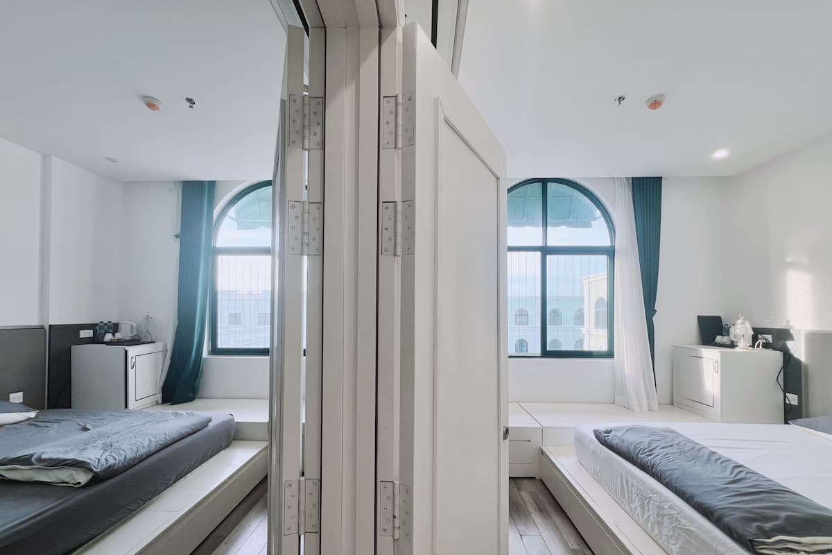 Habitación de hotel moderna con dos camas, un escritorio pequeño y una ventana con cortinas.