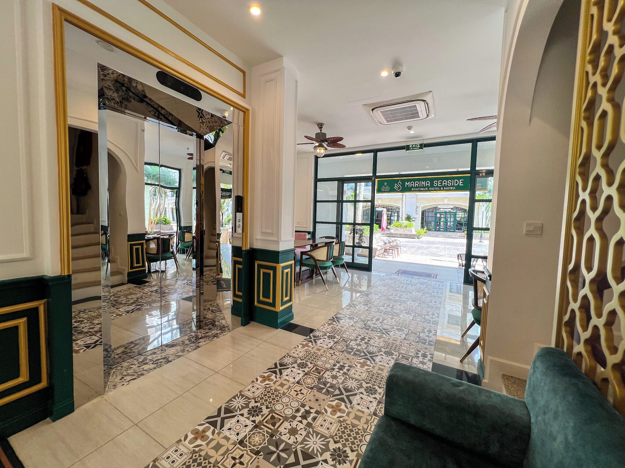 A hotel lobby with a marble floor, green and gold accents, and a view of the outside.