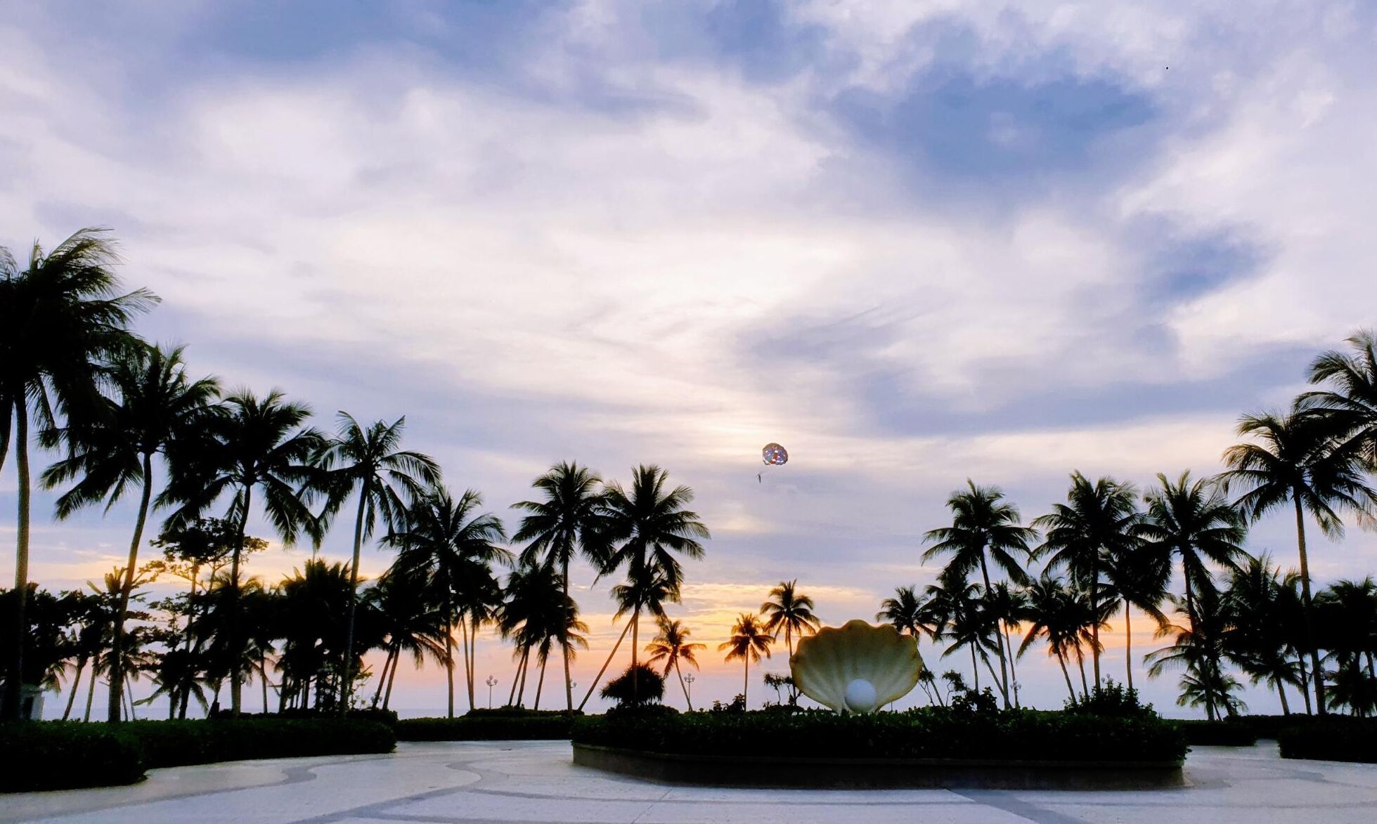 A sunset view with palm trees and a large decorative shell sculpture.