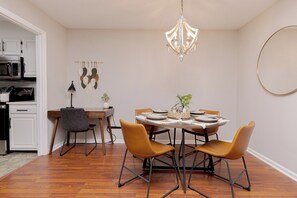 A dining area with a round table, four chairs, a chandelier, a wall-mounted circular mirror, and a kitchen in the background. - Convenient Stay | 3BR | Fenced Yard | Near RAFB (Warner Robins)