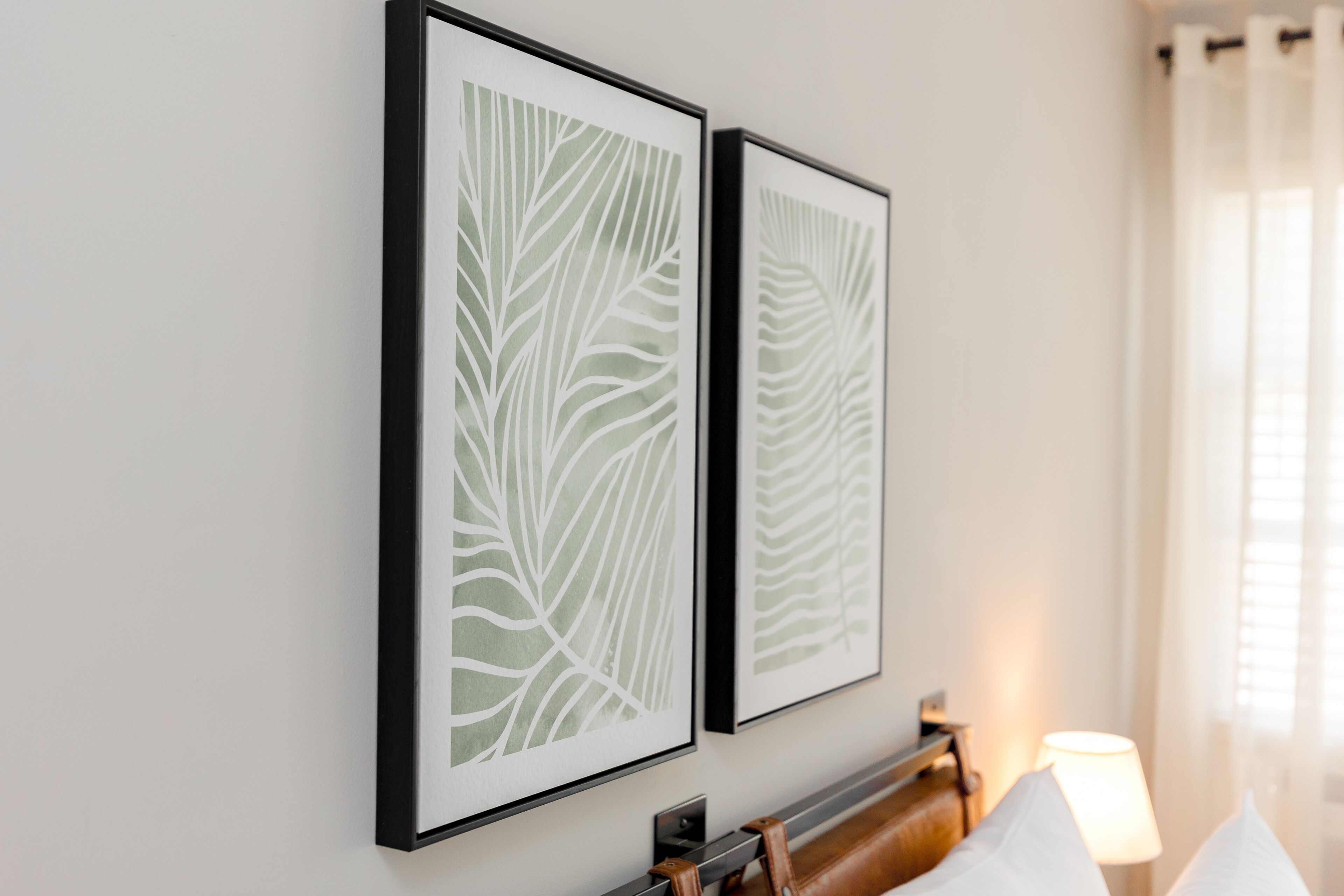 Two framed wall art pieces with leaf patterns, a wooden bench, and a lamp in a room.