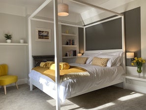 A four-poster canopy bed with a white frame, a bedside table with a lamp, and a bookshelf with books. - Isfyn, Boutique style cottage with stunning views in Llandudno.  (Penrhyn-side)