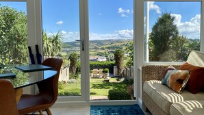 A room with a glass door leading to a garden, a sofa with cushions, a small table, and chairs. - Isfyn, Boutique style cottage with stunning views in Llandudno.  (Penrhyn-side)