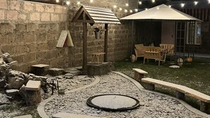 Un pati exterior amb parets de pedra, una xemeneia, seients i llums penjants.