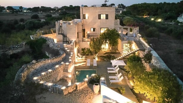 A modern villa with a swimming pool, outdoor seating, and a stone wall surrounding the property. - Cala Monaci Apartment (Favignana)