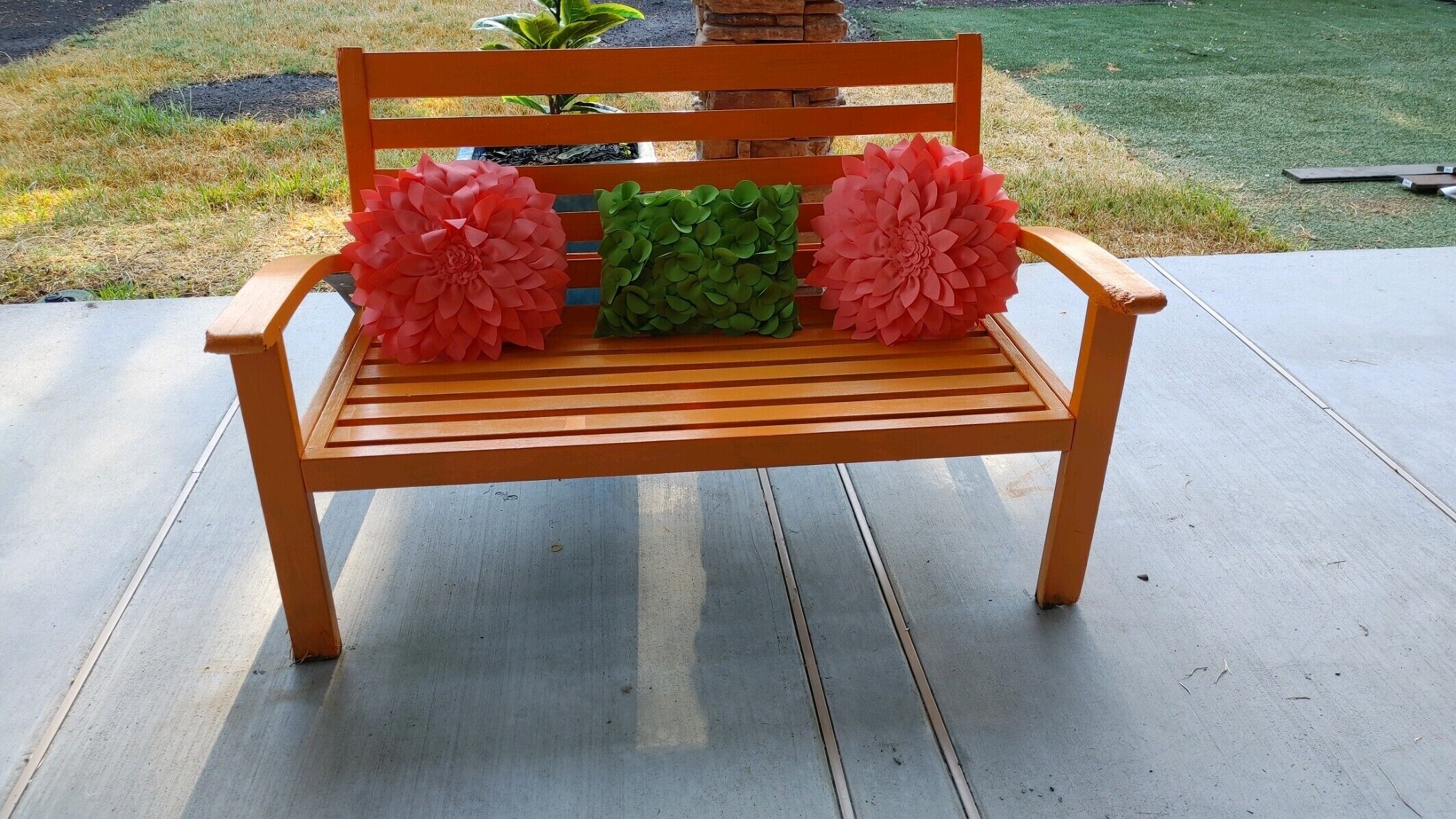 A wooden bench with two large pink paper flowers and one green paper flower on the seat.