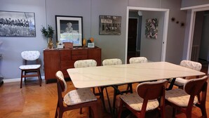 A dining area with a large rectangular table surrounded by six chairs with patterned cushions. There is a wooden cabinet with a 'Guest Book' sign on top. - Mid Century Modern Nights Dream (Houston)