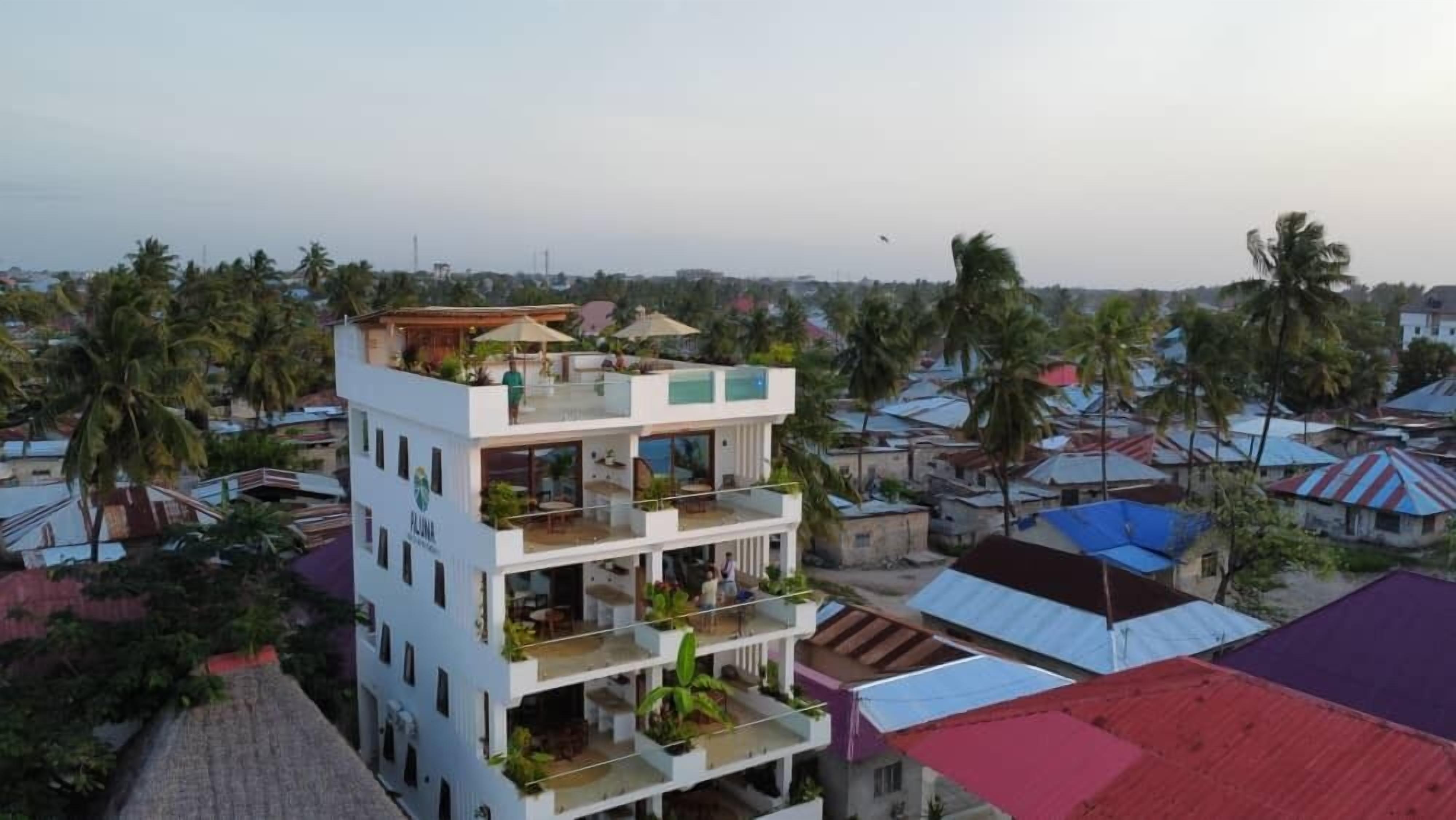 A multi-story hotel with balconies, outdoor seating, and a view of surrounding houses.