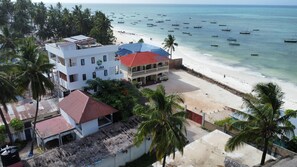 A beachfront hotel with multiple balconies, a beach view, and several boats in the water. - Aluna Beach Apartments (Nungwi)