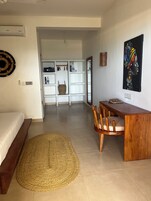 A modern hotel room with a bed, a wooden desk, a woven rug, a white wardrobe, and a painting on the wall.
