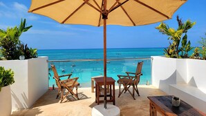 A balcony with a wooden table, two wicker chairs, and a large beige umbrella. - Aluna Beach Apartments (Nungwi)
