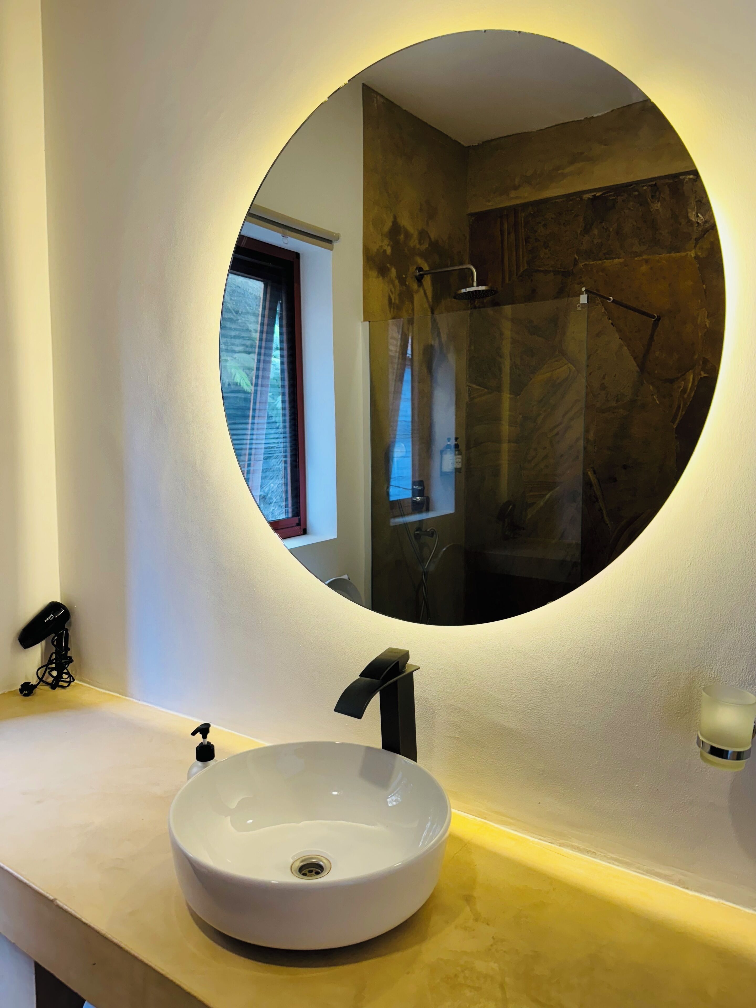 Ein Badezimmer mit einem runden Spiegel, einem weißen Waschbecken und einer Dusche.
