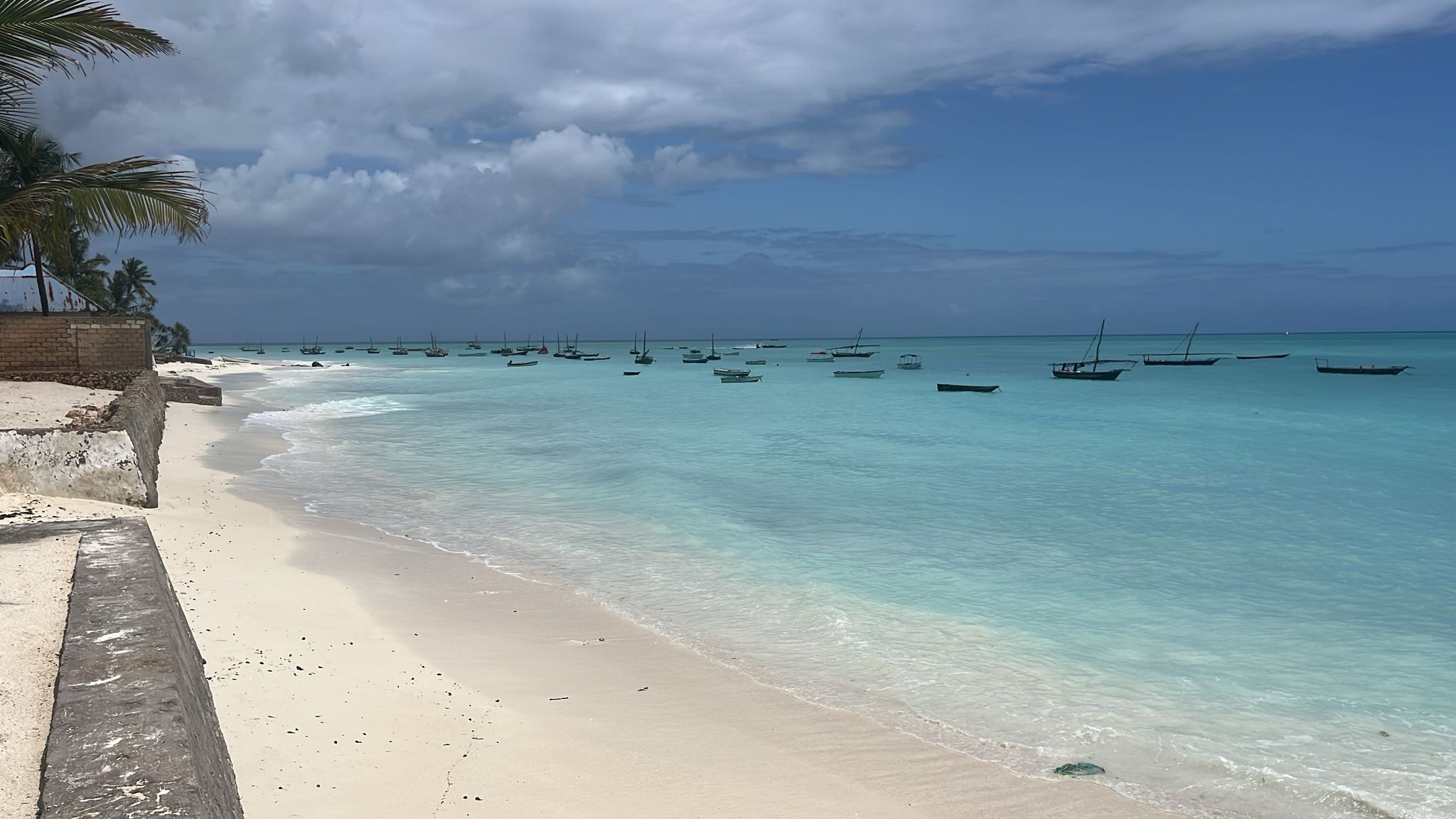 Una playa con agua turquesa cristalina, barcos y palmeras.