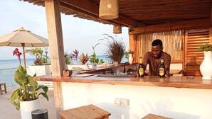 A wooden bar area with a view of the sea, potted plants, and a beachside setting. - Aluna Beach Apartments (Nungwi)