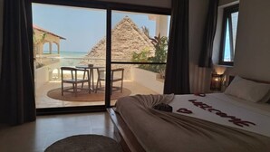 A hotel room with a bed, a balcony with a view of the sea and a pyramid, and a table with chairs. - Aluna Beach Apartments (Nungwi)