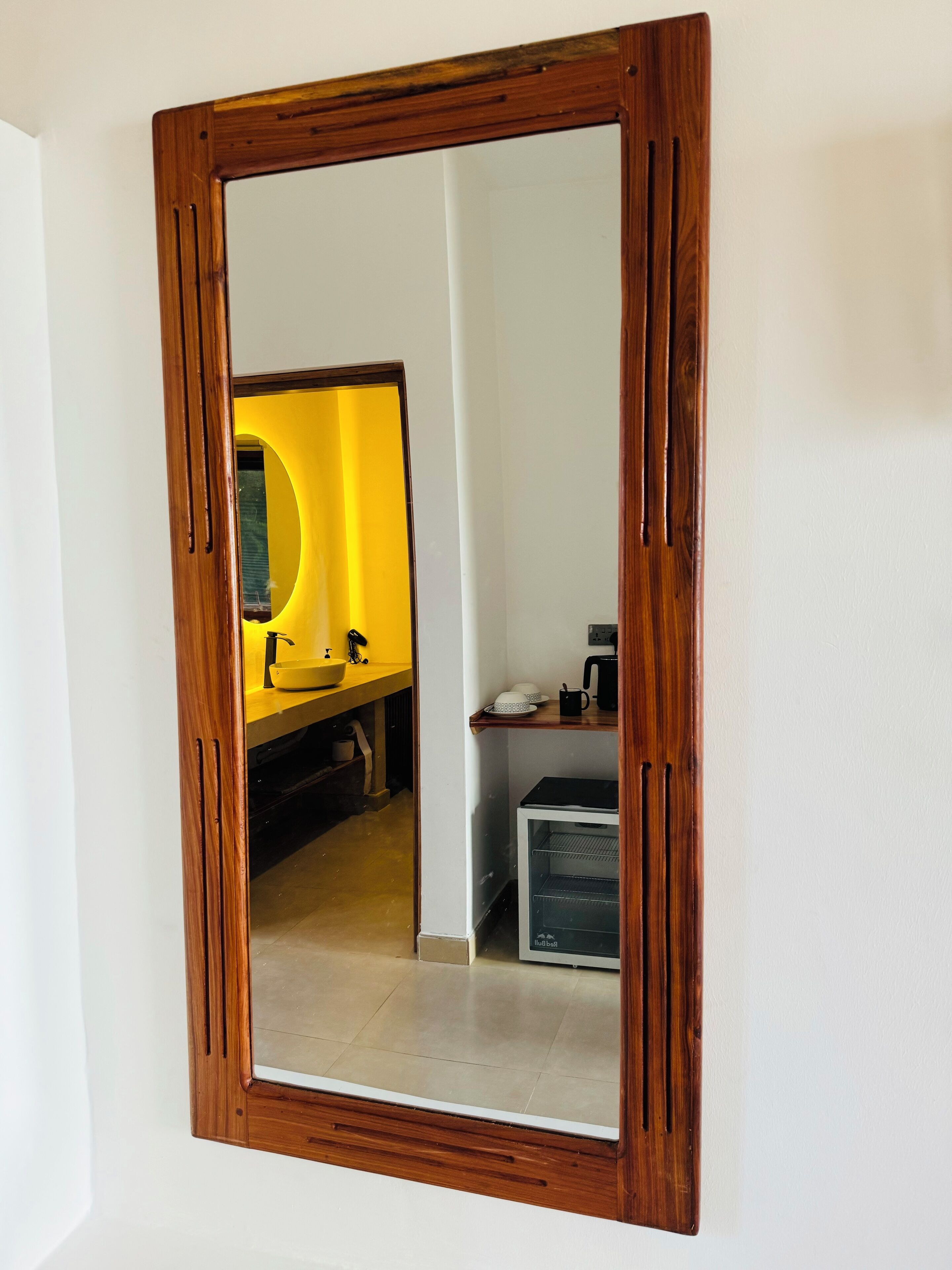 Ein Spiegel mit Holzrahmen, der ein Badezimmer mit einem gelben Waschbecken und einem schwarzen Schrank spiegelt.