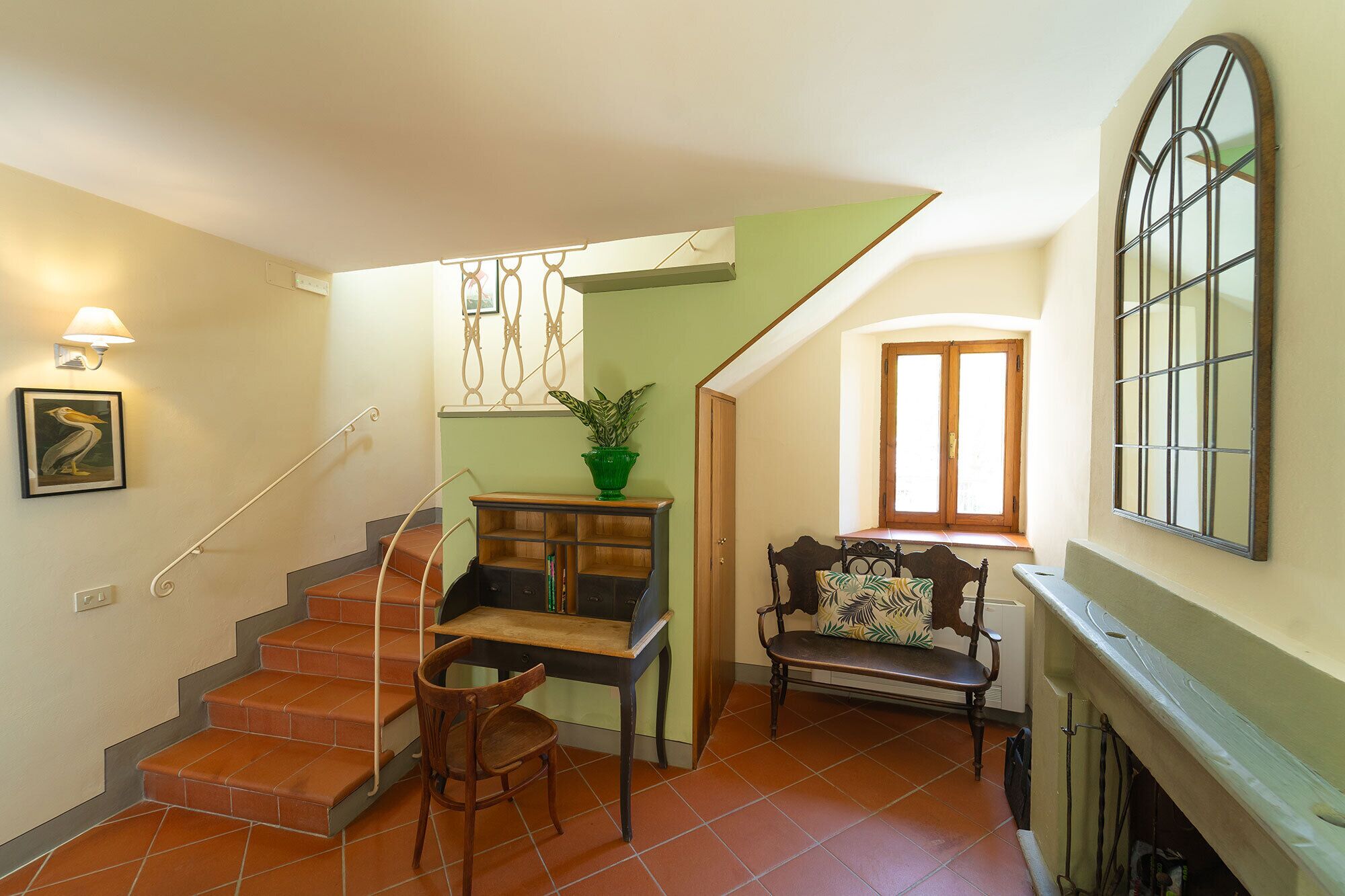 Una escalera con una silla de madera y una mesa, una pared verde y una ventana con vistas.