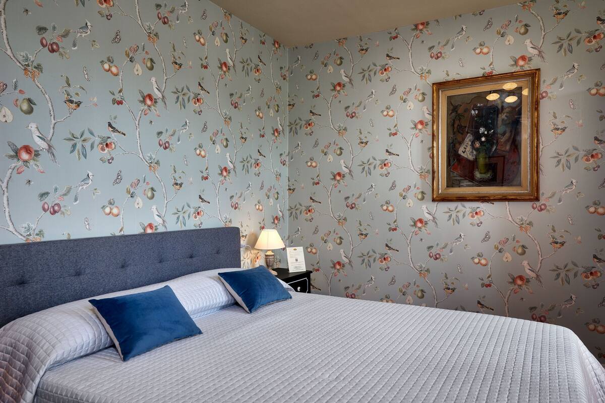 Une chambre à coucher avec un lit, des oreillers, une table de chevet, une lampe et un tableau encadré au mur.