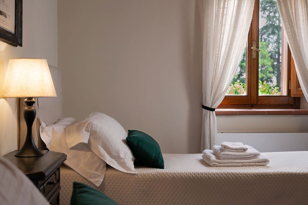 Un lit bien fait, avec des oreillers blancs et verts, une serviette pliée et une lampe sur une table de chevet.