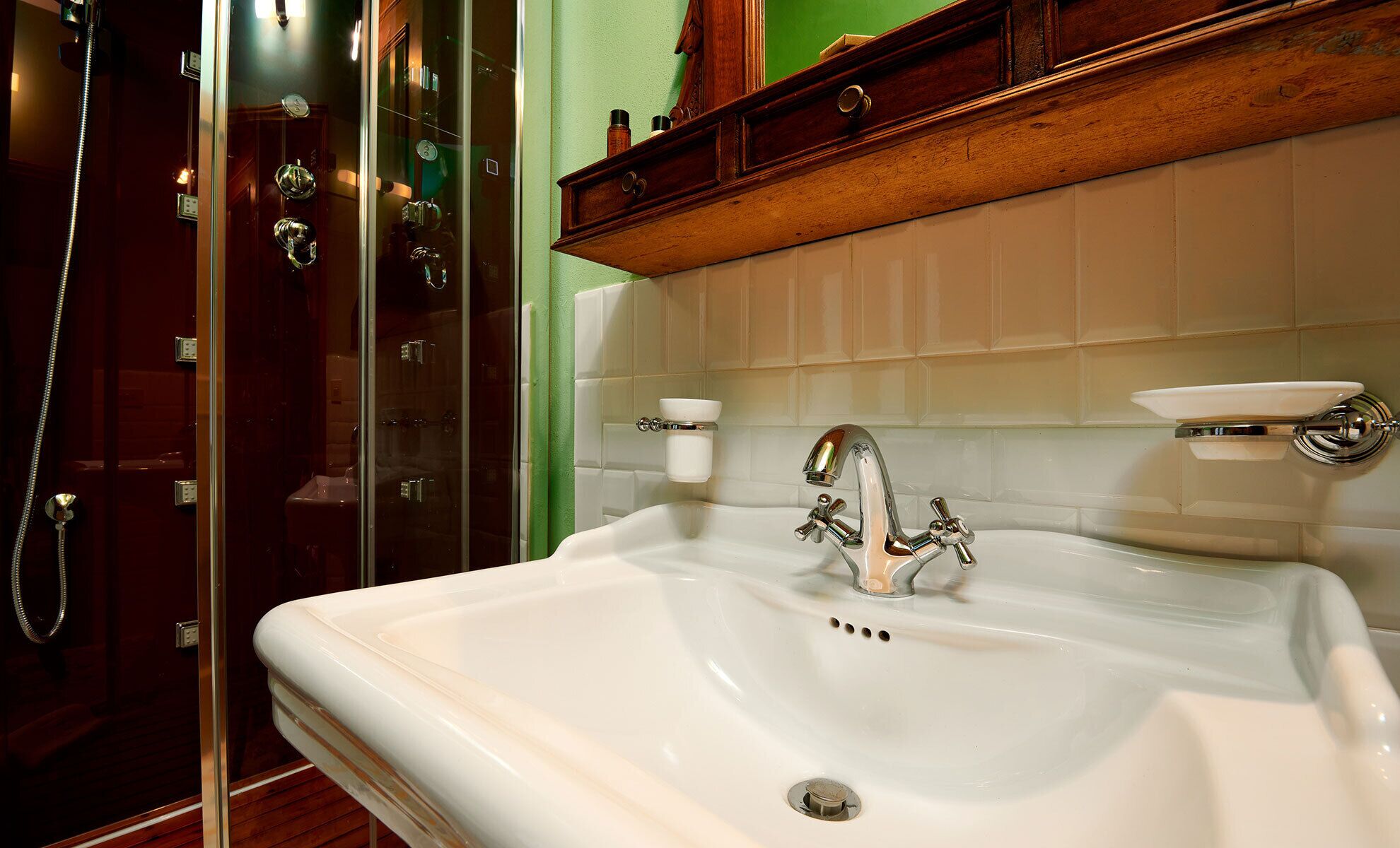 Un bagno con doccia vetrata, lavabo bianco con rubinetto cromato e mobile contenitore in legno con specchio sopra.